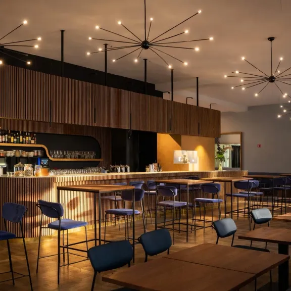 Moderne Bar mit Holztheke, blauen Stühlen und dekorativen Deckenleuchten.