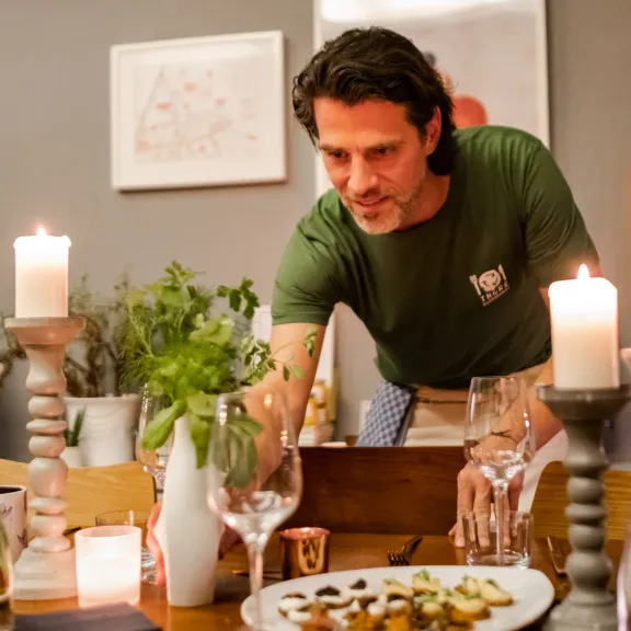 Mann deckt festlich gedeckten Tisch mit Kerzen und Speisen.