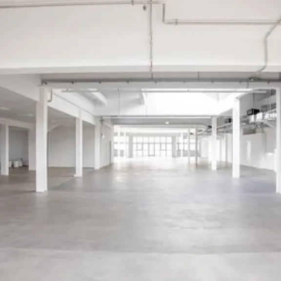 Leerer, heller Industriehallenraum mit weißen Säulen und Betonboden.