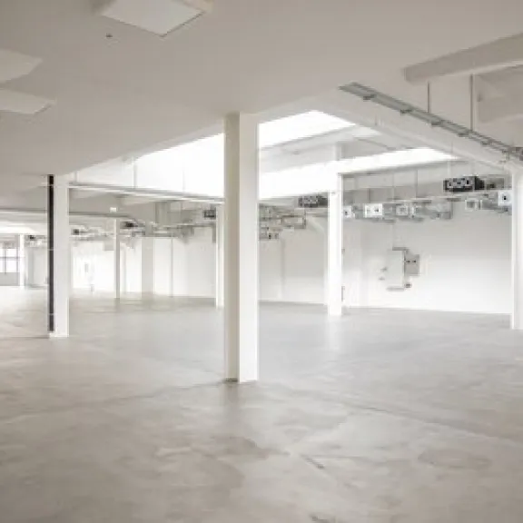 Leere, helle Industriehalle mit weißen Wänden und Betonboden.