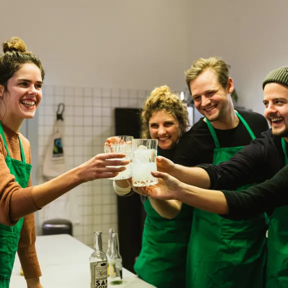Fünf Menschen mit grünen Schürzen stoßen lachend mit Getränken an.