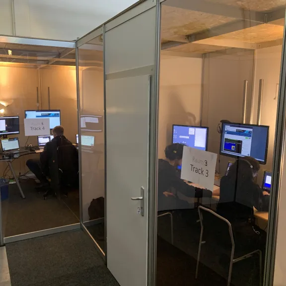 Mehrere Personen arbeiten an Computern in kleinen, abgetrennten Büroräumen.