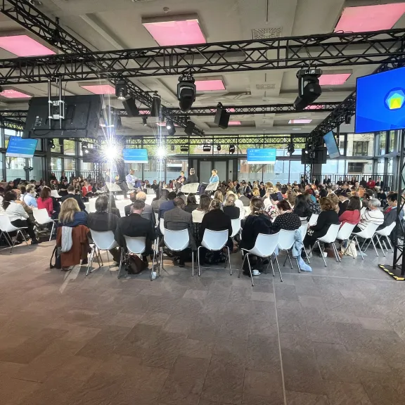Viele Menschen sitzen in einem modernen Konferenzraum und hören einer Podiumsdiskussion zu.