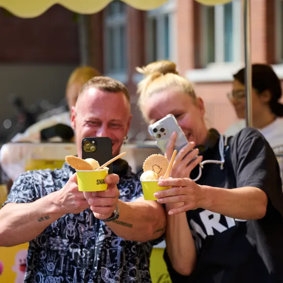 Zwei lachende Personen machen ein Selfie mit Eisbechern in der Hand.