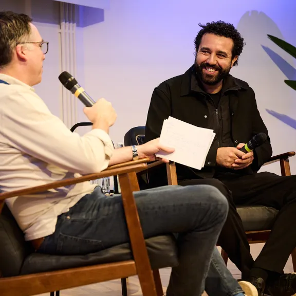 Zwei Männer sitzen auf Stühlen und unterhalten sich, einer hält ein Mikrofon.