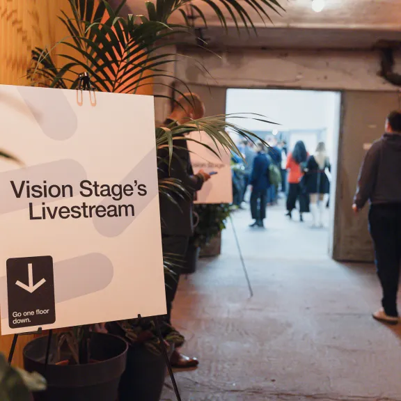 Schild mit „Vision Stage’s Livestream“, Menschen gehen durch einen Flur.