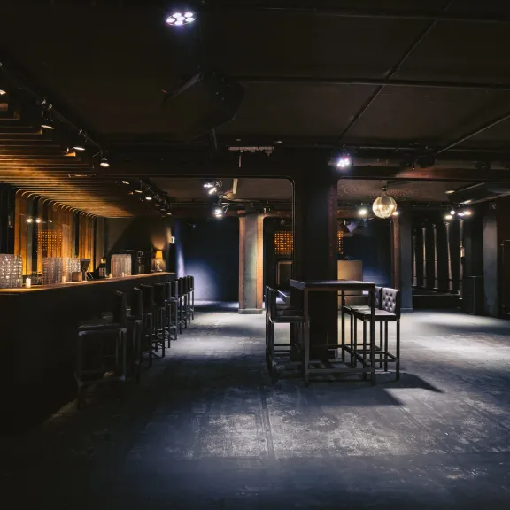 Dunkle Bar mit Stehtischen, Hocker und warmer Beleuchtung