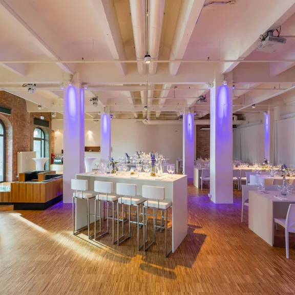 Modern eingerichteter Veranstaltungsraum mit lila Beleuchtung und Holzboden.