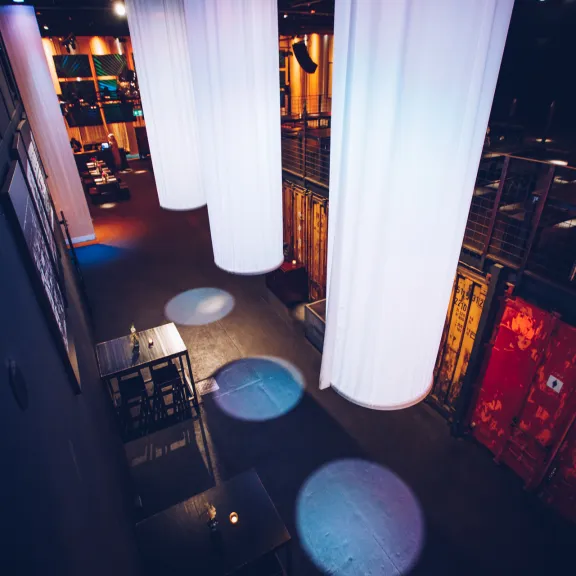 Leerer, modern beleuchteter Veranstaltungsraum mit weißen Stoffbahnen und roten Containern.