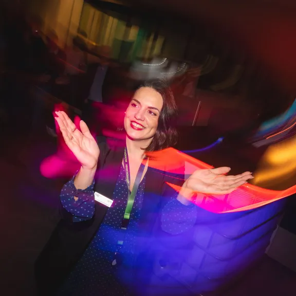 Frau klatscht und lächelt in bunt beleuchteter, verschwommener Umgebung.