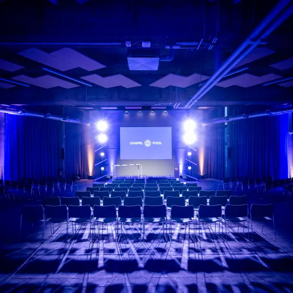 Konferenzraum mit leeren Stühlen und blau beleuchteter Bühne
