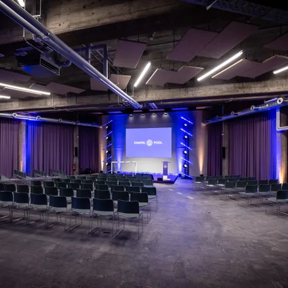 Leerer Konferenzsaal mit Bühnenbeleuchtung in Blau und Reihen von Stühlen.