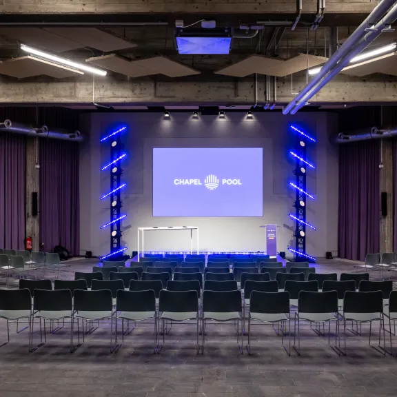 Leerer Konferenzsaal mit Bühne, Stühlen und lila Beleuchtung.