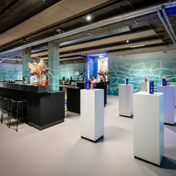 Moderner Raum mit Bar, hohen Tischen und dekorativer Beleuchtung.