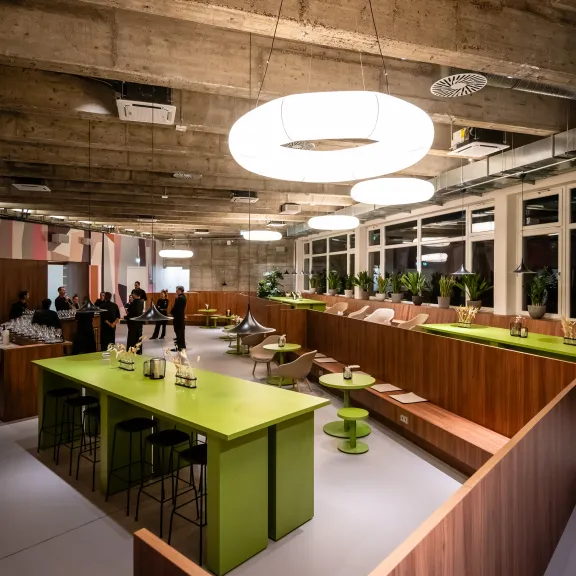Modernes Büro mit grünen Tischen, Holzabtrennungen und runden Deckenleuchten