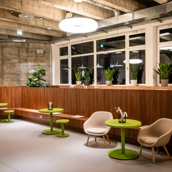 Modernes Café mit grünen Tischen, Holztrennwänden und vielen Pflanzen.