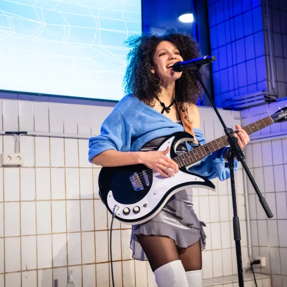 Frau spielt E-Gitarre und singt auf einer Bühne mit blauen Lichtern