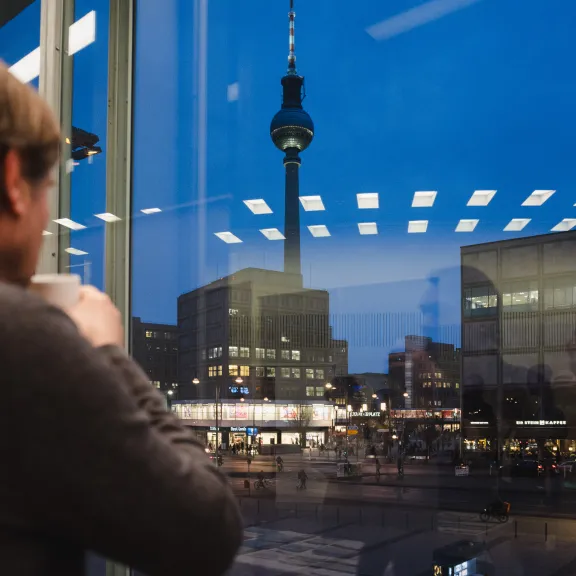 Mann schaut aus dem Fenster mit Blick auf den Fernsehturm