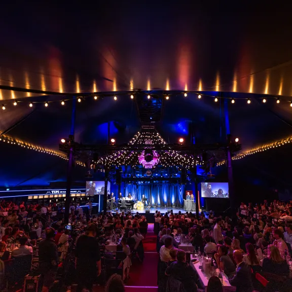 Der illuminierte, voll besuchte Saal im TIPI AM KANZLERAMT, Blick auf die Bühne davor Gäste an Tischen verteilt, nicht erkenntlich