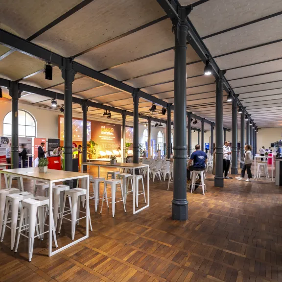 Großer heller Ausstellungsraum mit Ständen, Tischen und wenigen Menschen.