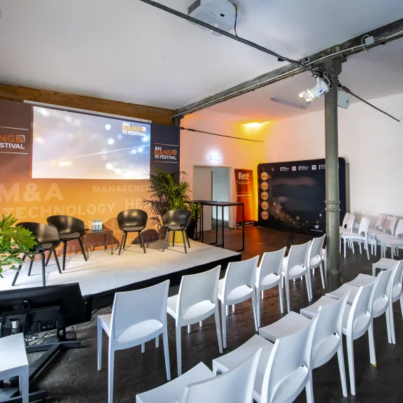 Konferenzraum mit leeren weißen Stühlen und Bühne, Pflanzen und Projektor.