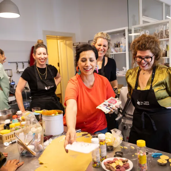 Gruppe fröhlicher Menschen kocht zusammen in einer hellen, modernen Küche.