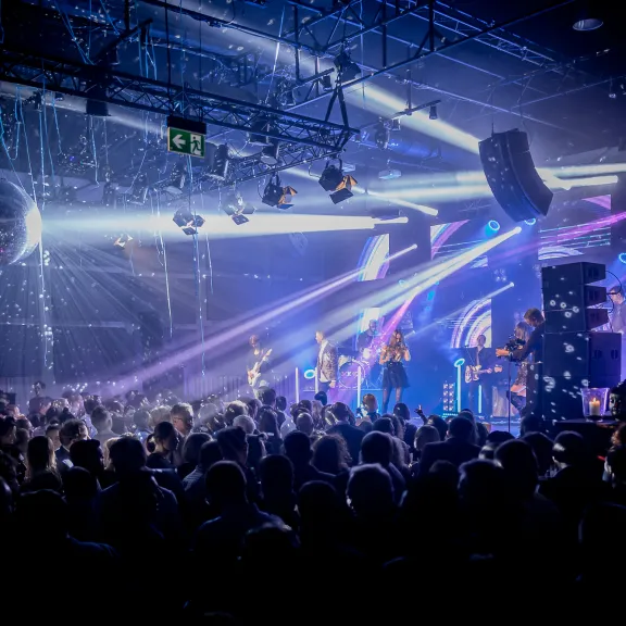 Konzertbühne mit Band, Lichtershow und großem Publikum in dunkler Halle
