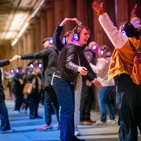 Teilnehmende mit leuchtenden Funkkopfhörern tanzen und interagieren während einer Silent Disco Tour im urbanen Außenraum bei Nacht.