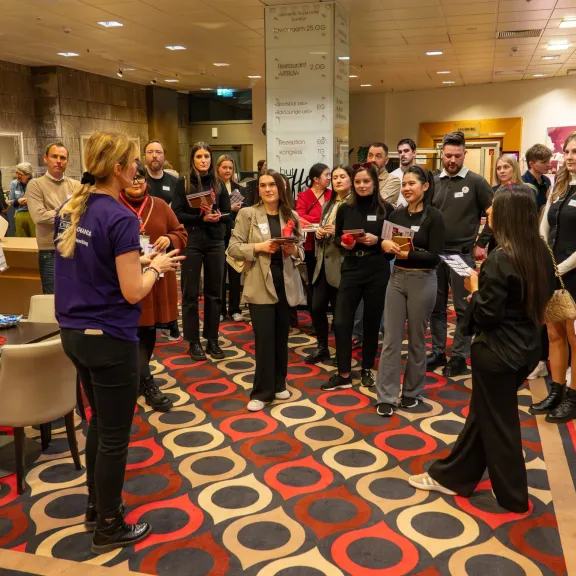 Gruppe von Menschen hört einer Frau in einem Konferenzraum aufmerksam zu.
