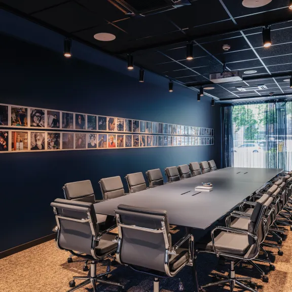 Moderner Konferenzraum mit langem Tisch, vielen Stühlen und Fotos an der Wand.
