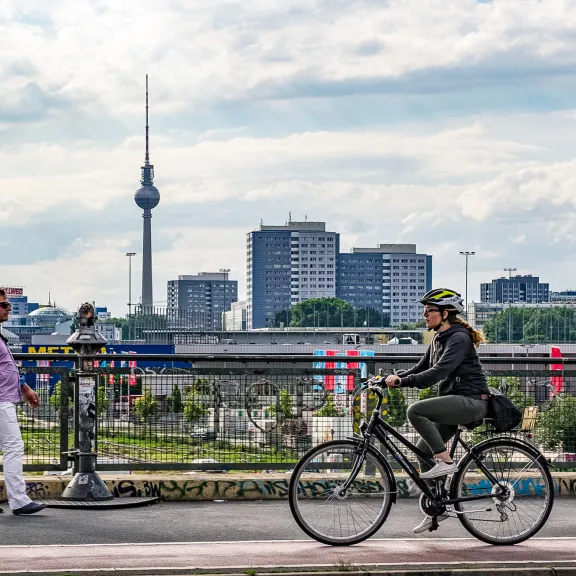 Radfahrerin und Fußgänger auf Brücke, Berliner Fernsehturm im Hintergrund.