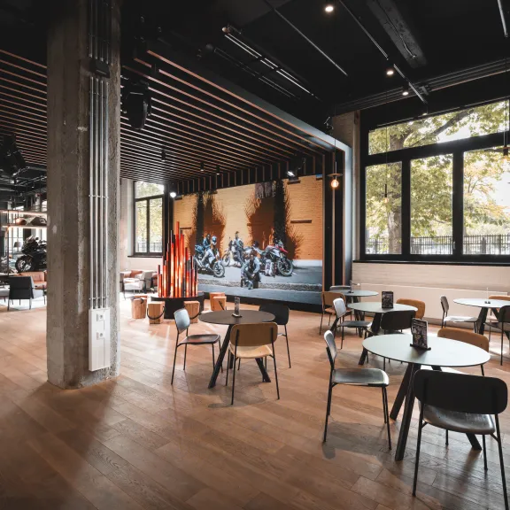 Modernes Café mit Holzboden, großen Fenstern und Motorraddeko an der Wand.