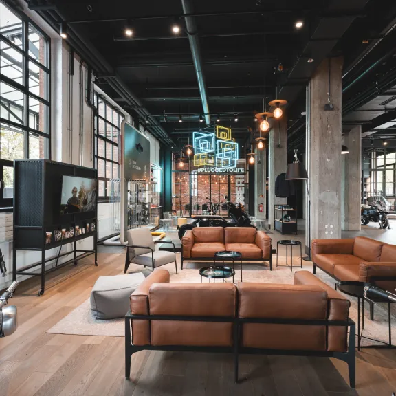 Moderner, heller Loftraum mit braunen Ledersofas, großen Fenstern und Industriecharakter.