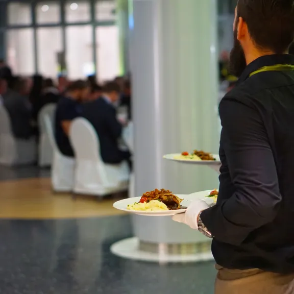 Kellner trägt zwei Teller zu festlich gedeckten Tischen mit Gästen.