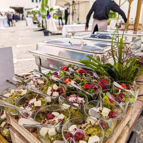 Buffet mit kleinen Gläsern Salat und Käse, draußen bei einer Veranstaltung angerichtet.