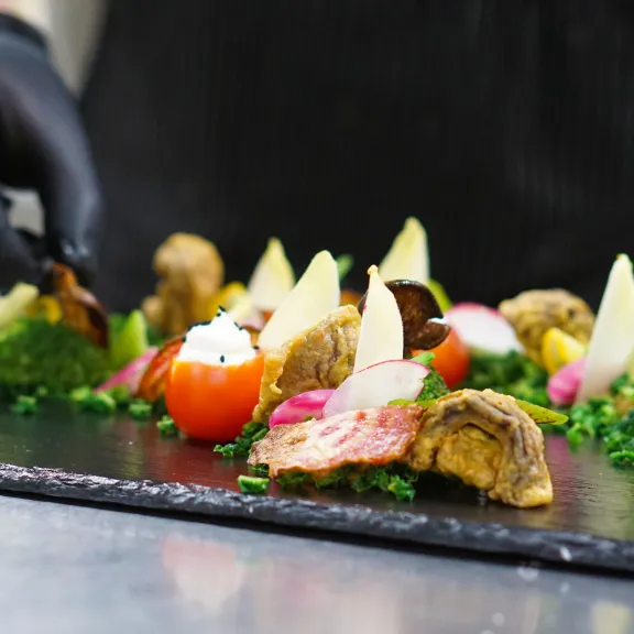 Koch arrangiert kunstvoll buntes Fingerfood auf schwarzer Platte.