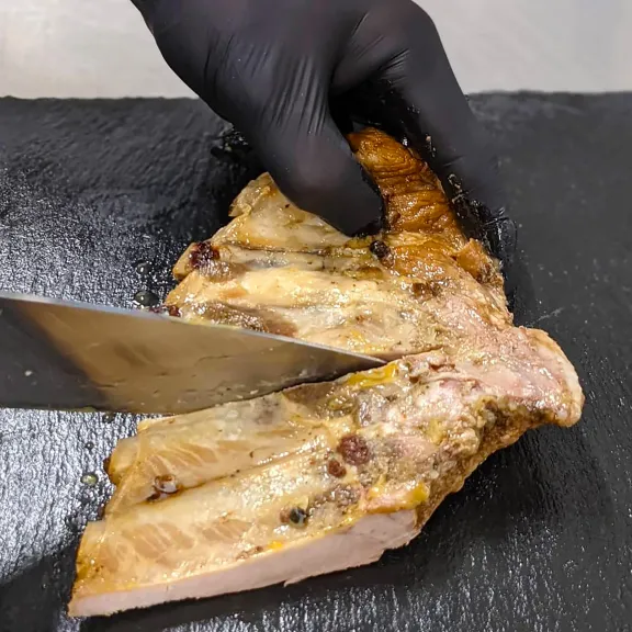 Koch schneidet gebratene Rippchen auf schwarzem Brett.