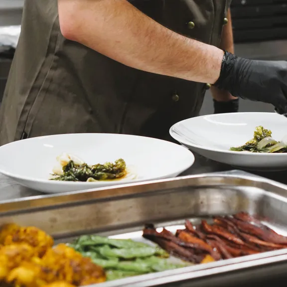 Koch richtet Speisen auf weißen Tellern in einer Restaurantküche an.