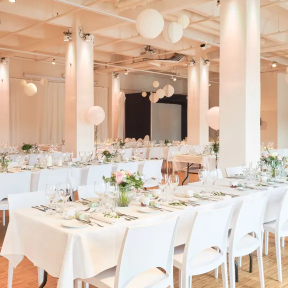 Festlich dekorierter großer Saal mit langen, weiß gedeckten Tischen und Blumen.