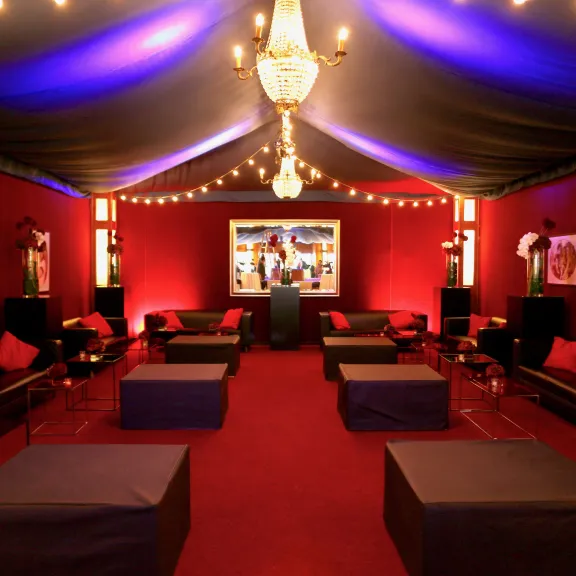 Elegant eingerichteter Lounge-Bereich mit roten Wänden, Sofas und Kronleuchter.