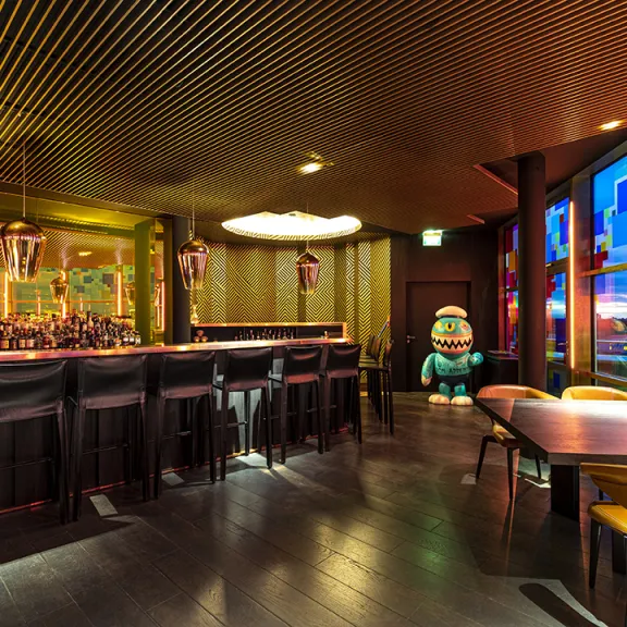 Moderne Bar mit goldener Decke, buntem Fenster und stilvollen Sitzbereichen.