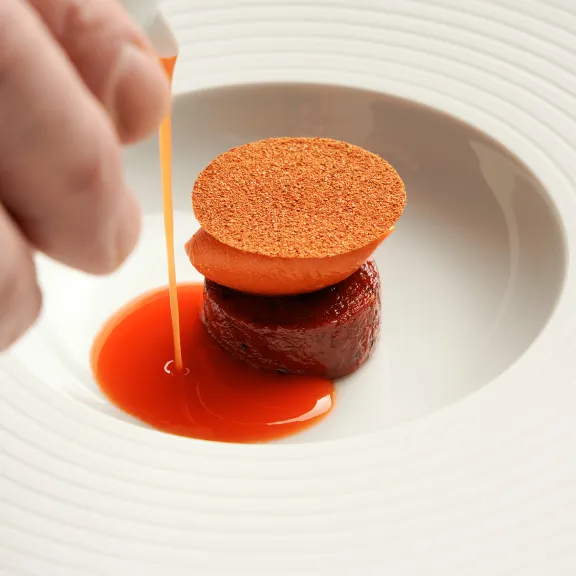 Gourmetgericht mit roter Sauce wird um ein rundes Element auf einem weißen Teller gegossen.