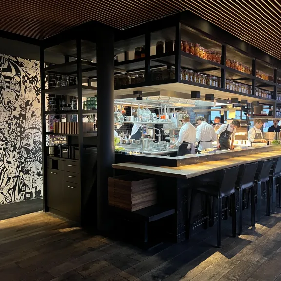 Moderne Bar mit offenen Regalen, Köche arbeiten hinter dem Tresen, gedämpftes Licht.