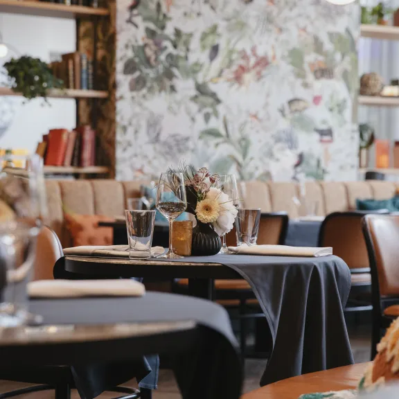 Modernes Restaurant mit gedeckten Tischen, Blumenvasen und gemütlicher Atmosphäre.
