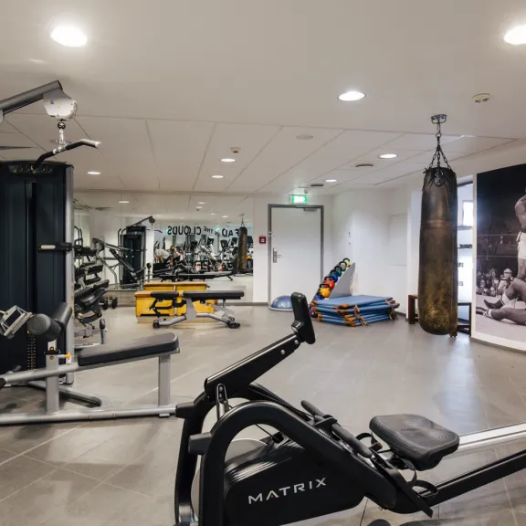 Fitnessraum mit Kraftgeräten, Boxsack und großem Sportposter an der Wand.