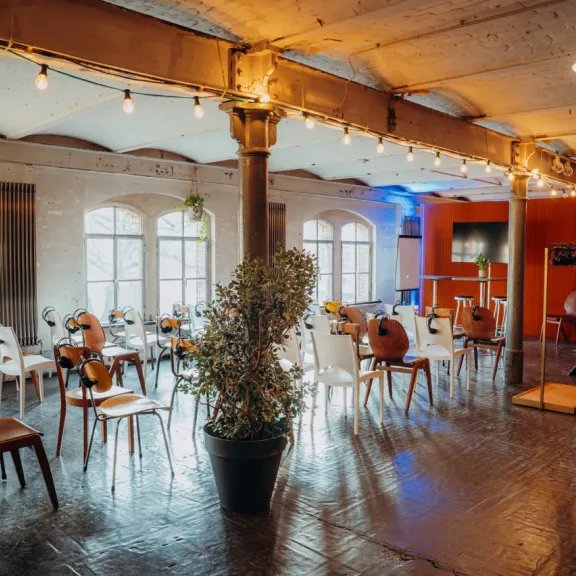 Heller Veranstaltungsraum mit Stühlen, Pflanzen und Lichterketten.