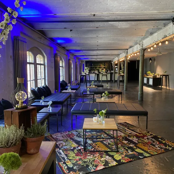 Modern eingerichteter Loungebereich mit Sofas, Tischen, Pflanzen und bunter Beleuchtung.