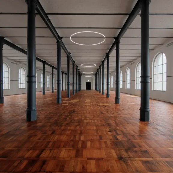 Leerer, heller Saal mit Holzboden, schwarzen Säulen und großen Fenstern