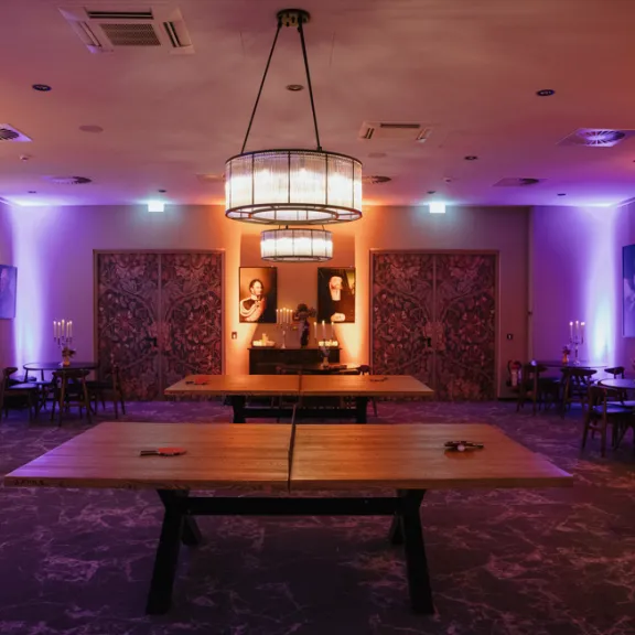 Stimmungsvoll beleuchteter Raum mit Tischen, Stühlen und bunten Wandlichtern.