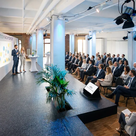 Menschen in Businesskleidung sitzen bei einer Präsentation in einem modernen Konferenzraum.